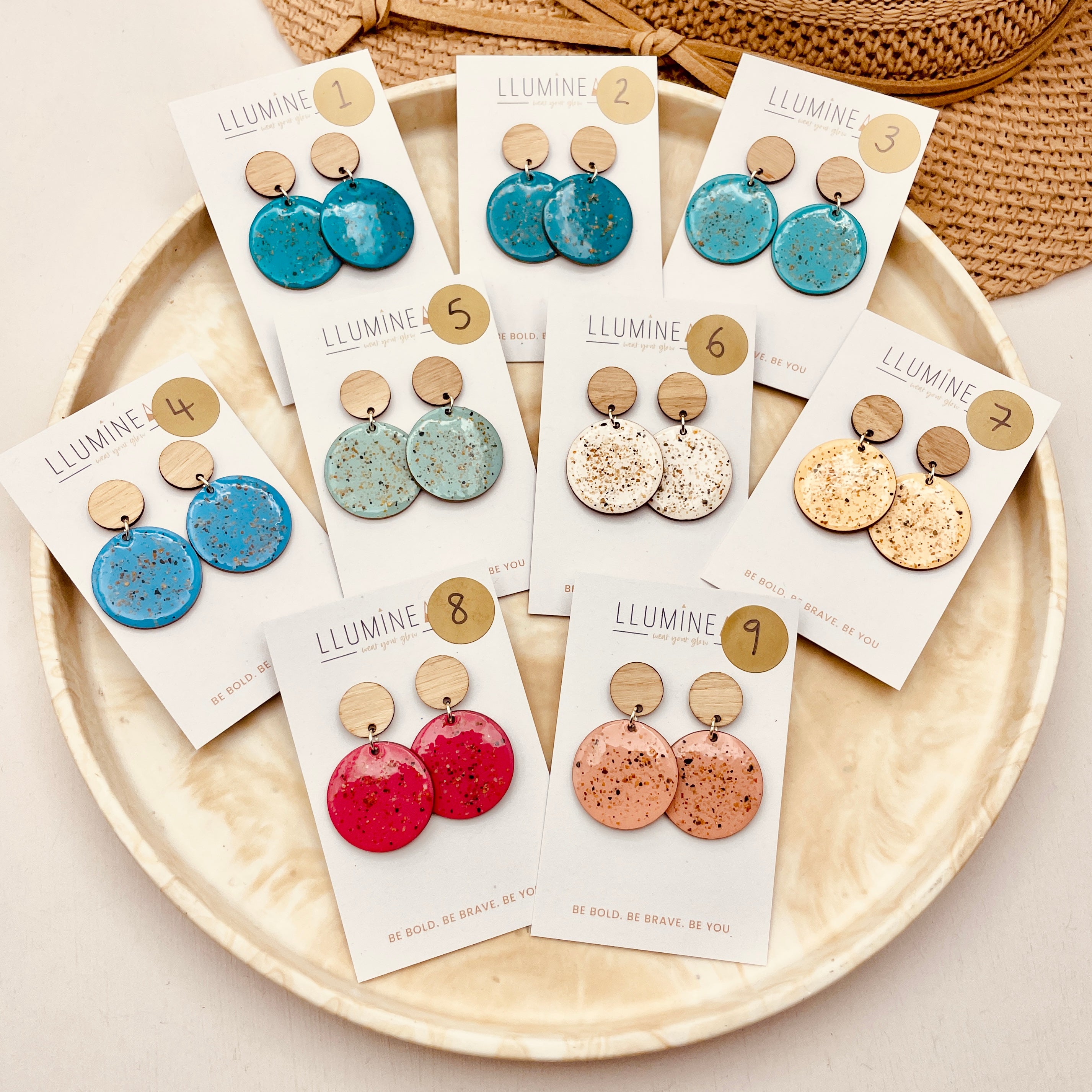 Set of bright stylish earrings on cards with 'Lluminear' branding on a beige plate.