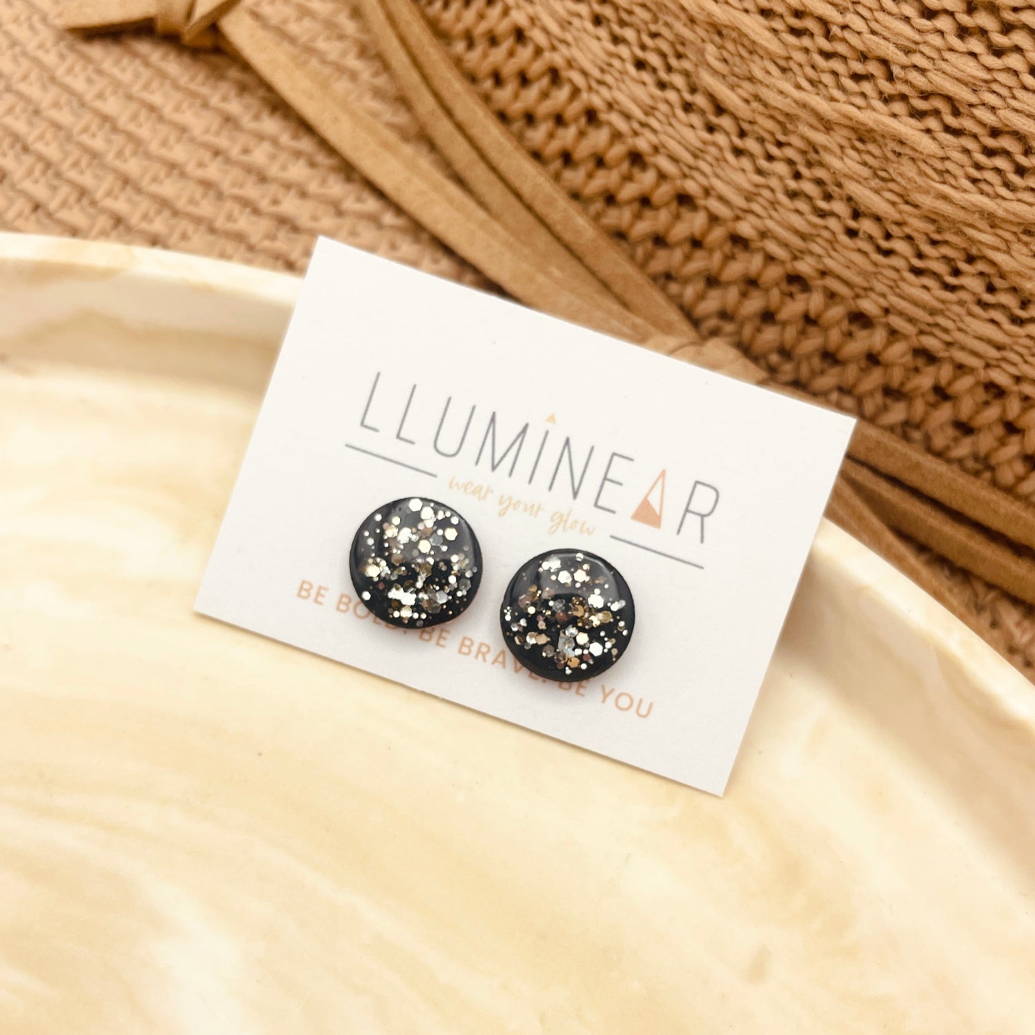 Pair of black glittery earrings on a 'Lumineur' branded card with a beige fabric background.