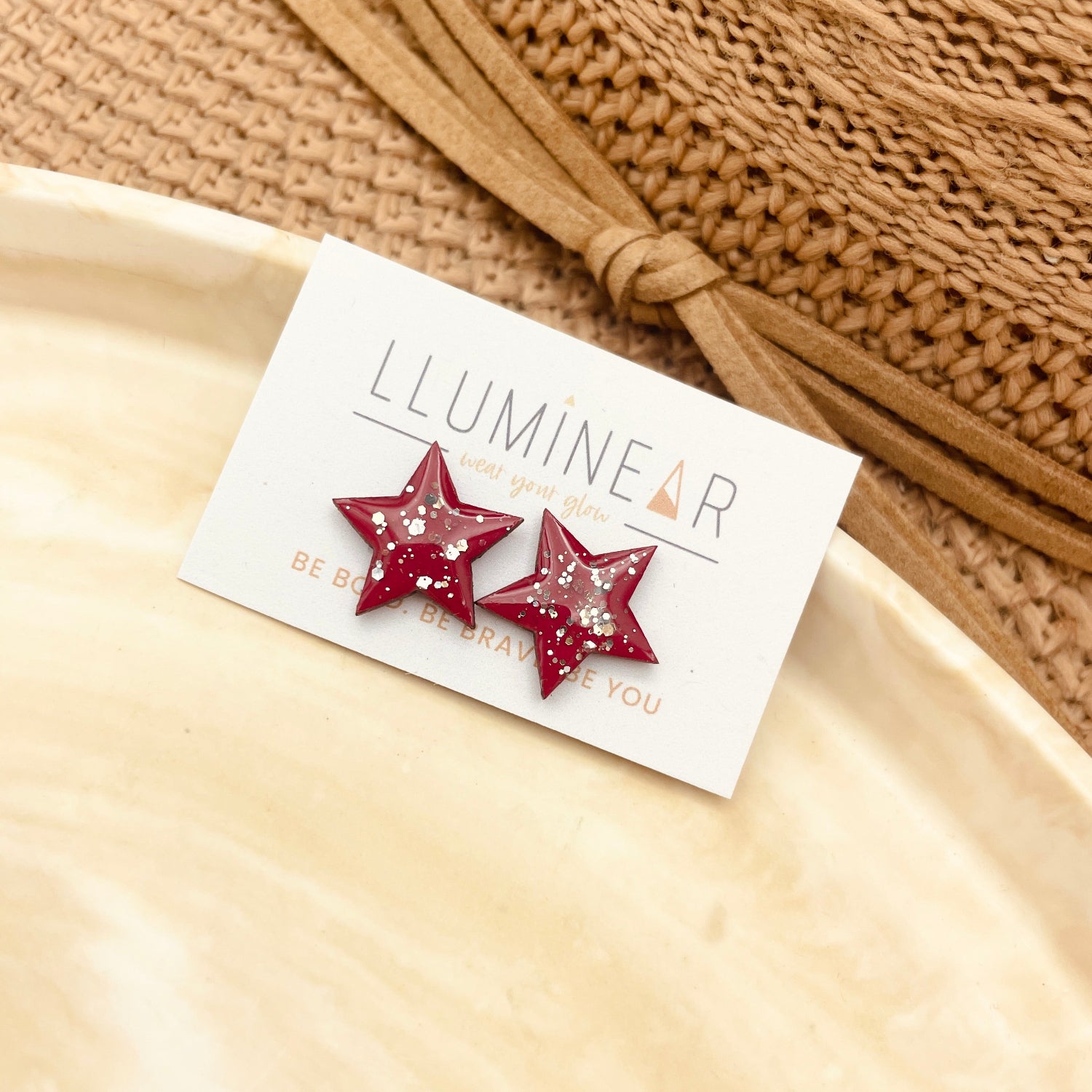 Star-shaped earrings on a card with 'LLUMINEAR' branding, placed on a beige surface.