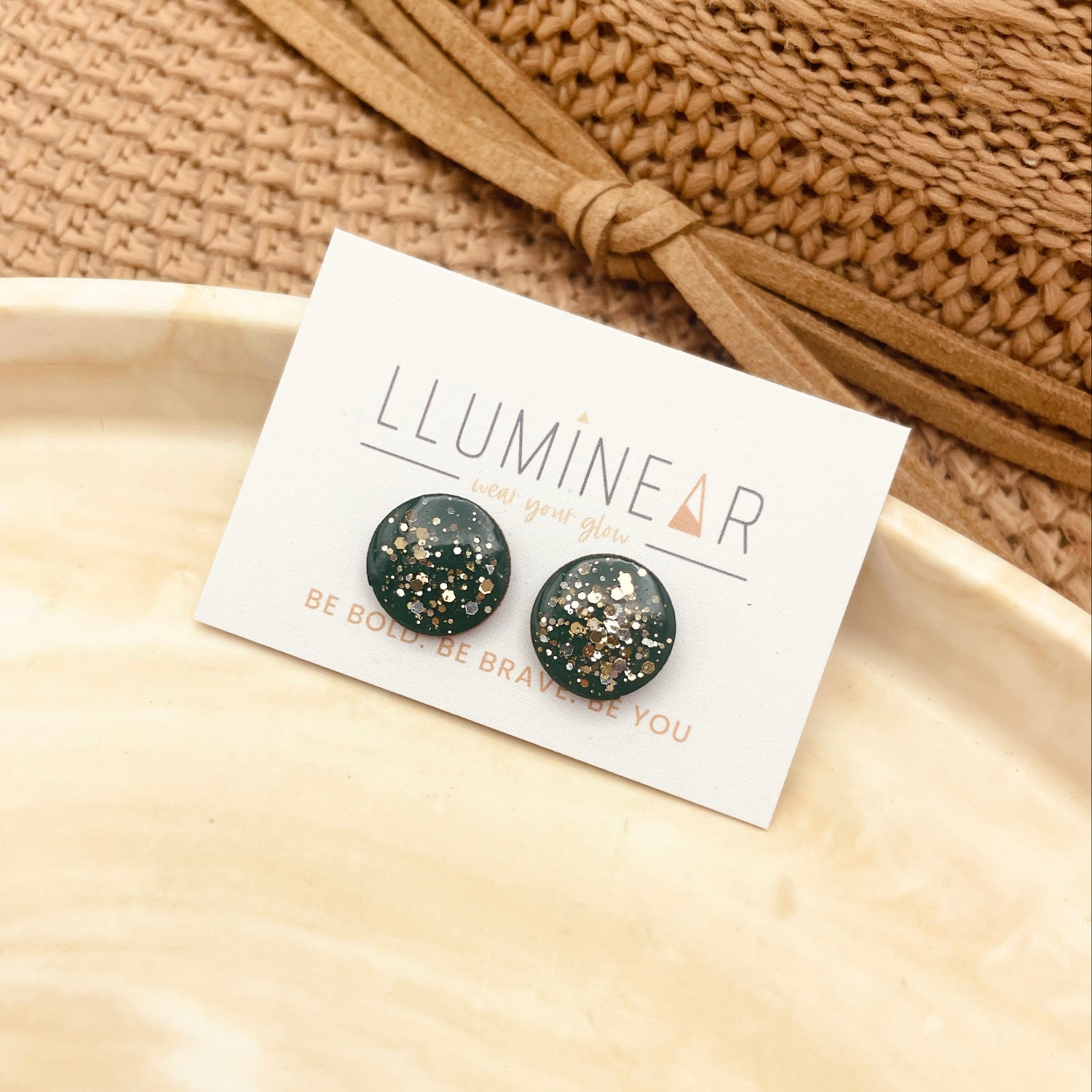 Pair of black and gold speckled earrings on a 'Lluminear' branded card with a beige background.