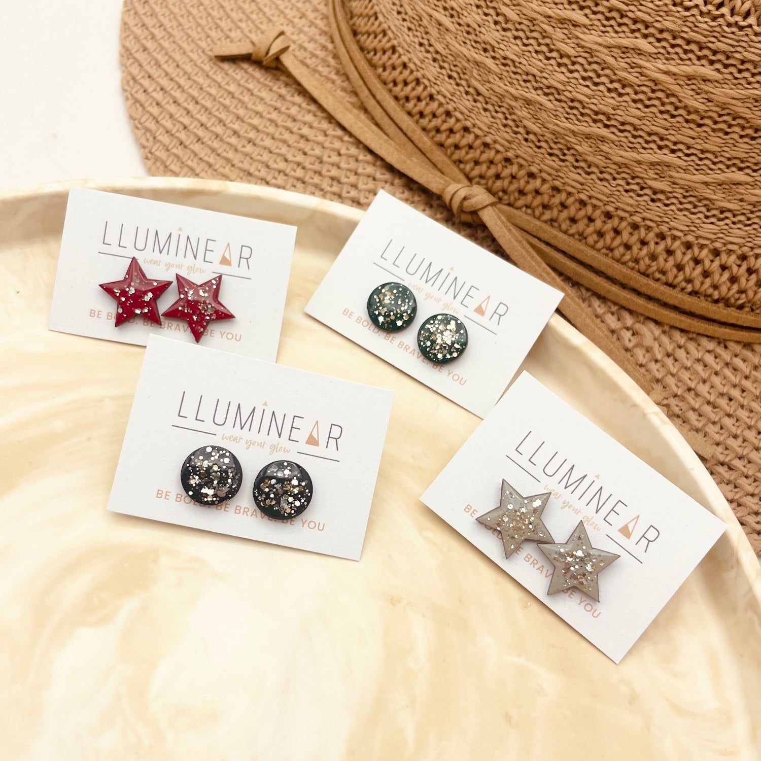 Star-shaped earrings on Lluminear branded cards with a beige hat in the background.