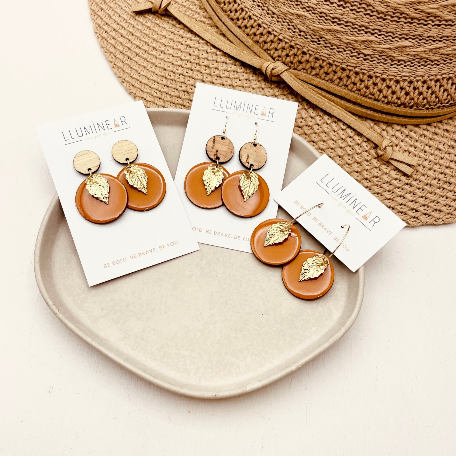 Pair of orange gold leaf earrings on display with packaging on a neutral background
