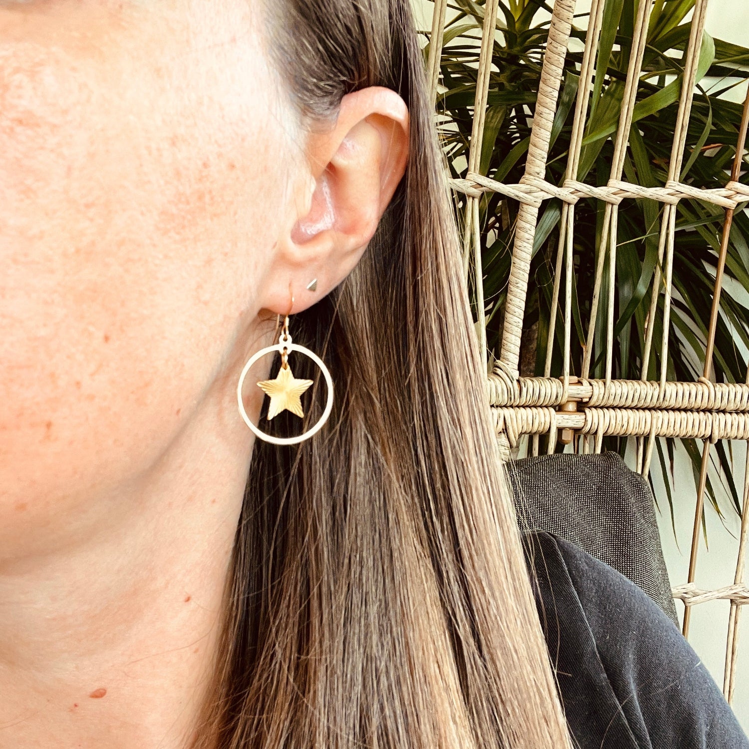 Close-up of a person wearing a gold hoop earring with a star pendant, sitting in a wicker chair.