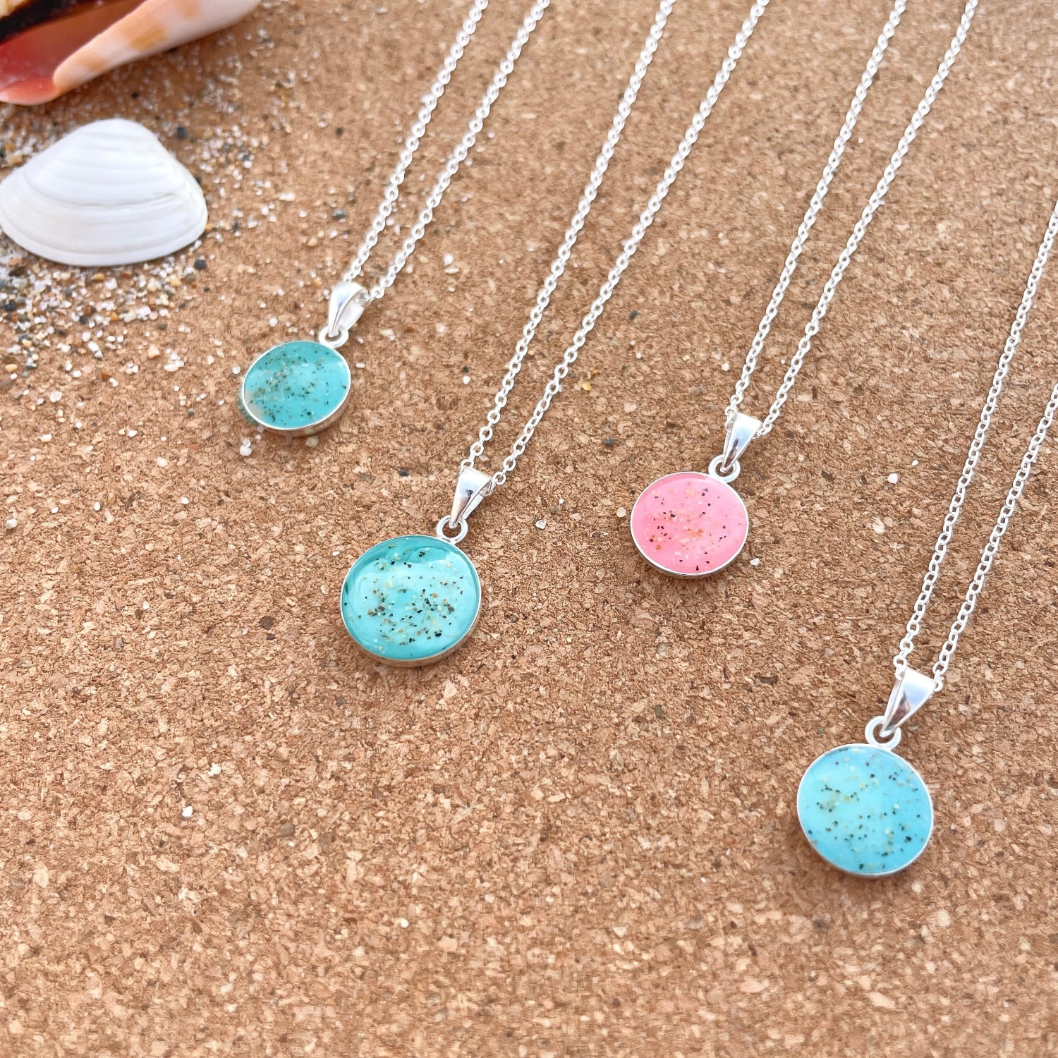 Three necklaces with round, colorful pendants on a sandy surface.