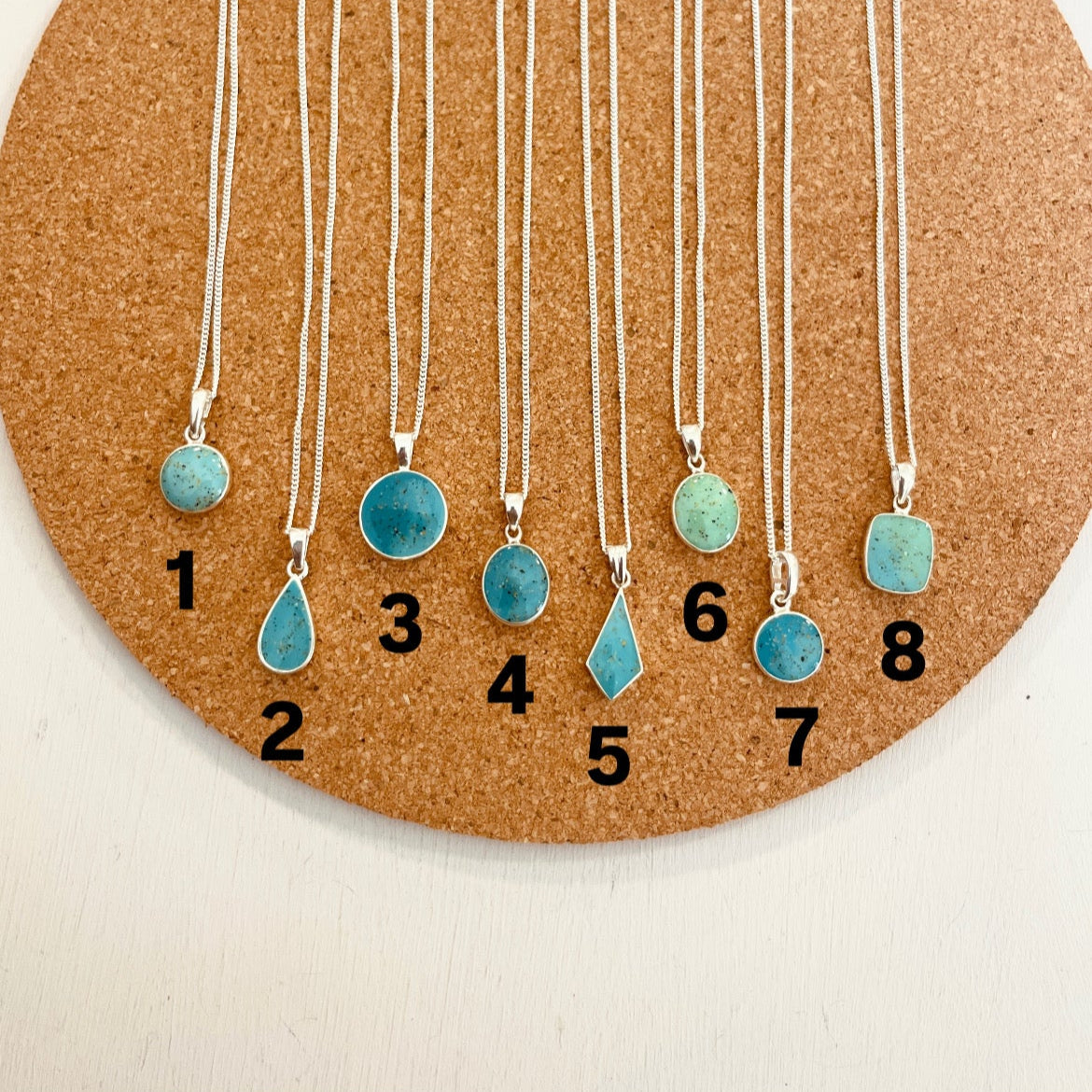 Set of turquoise pendant necklaces on a cork board with numbers