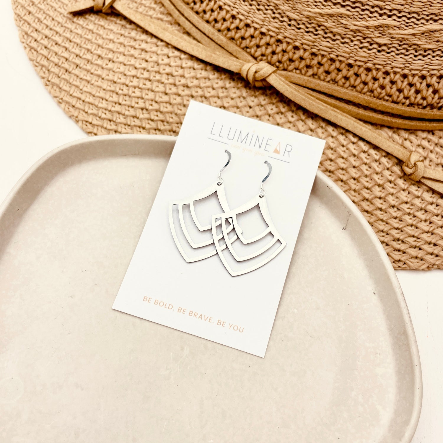 Earring card with earrings on a white plate next to a woven hat