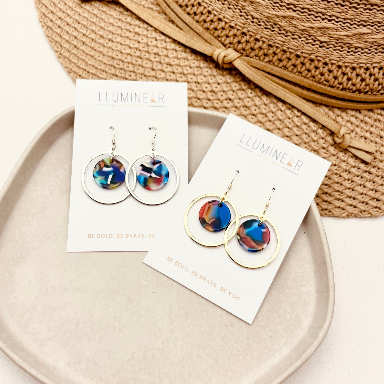 Colorful earrings on display with their packaging on a plate, against a neutral background.