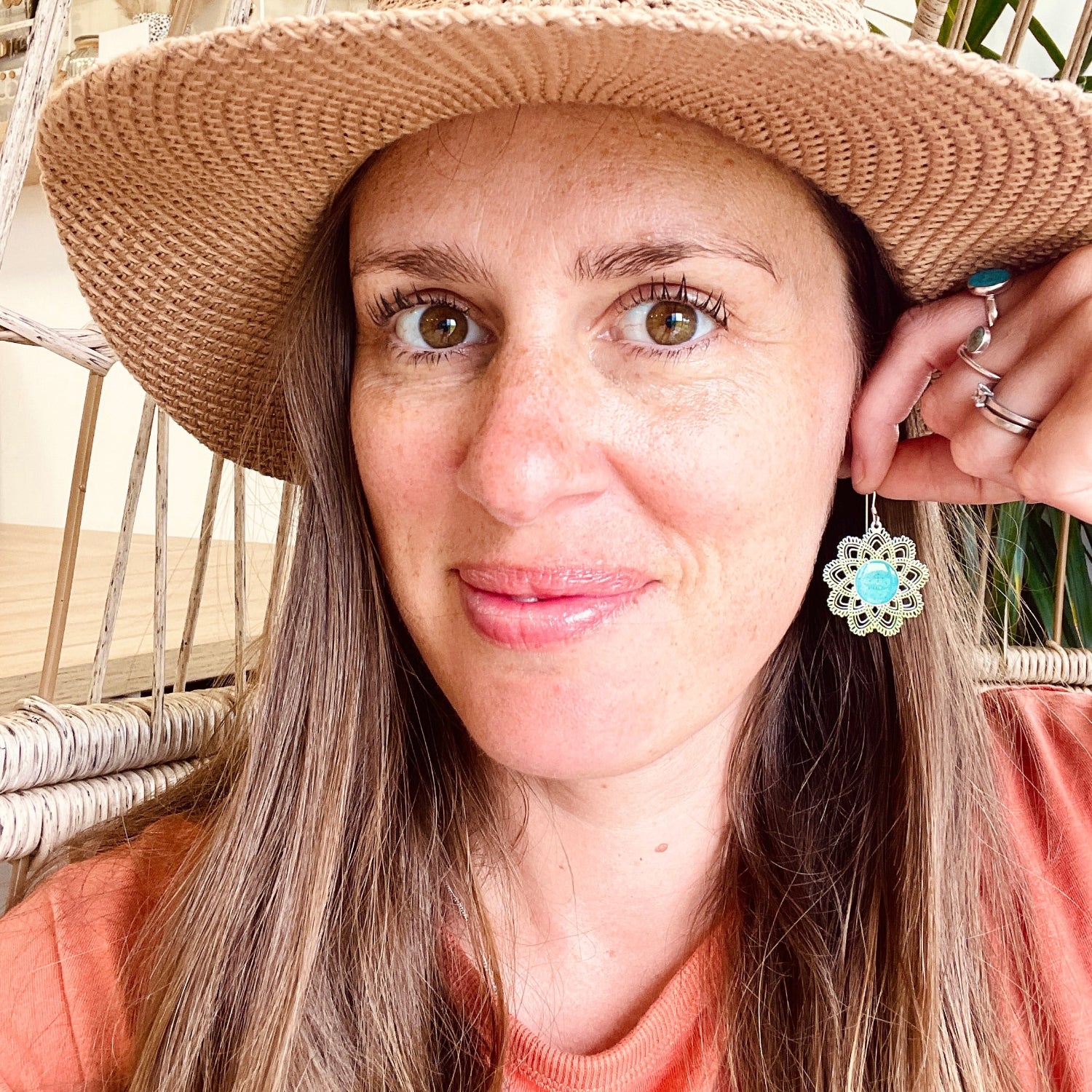 Woman wearing a straw hat and floral earrings, sitting in a wicker chair.