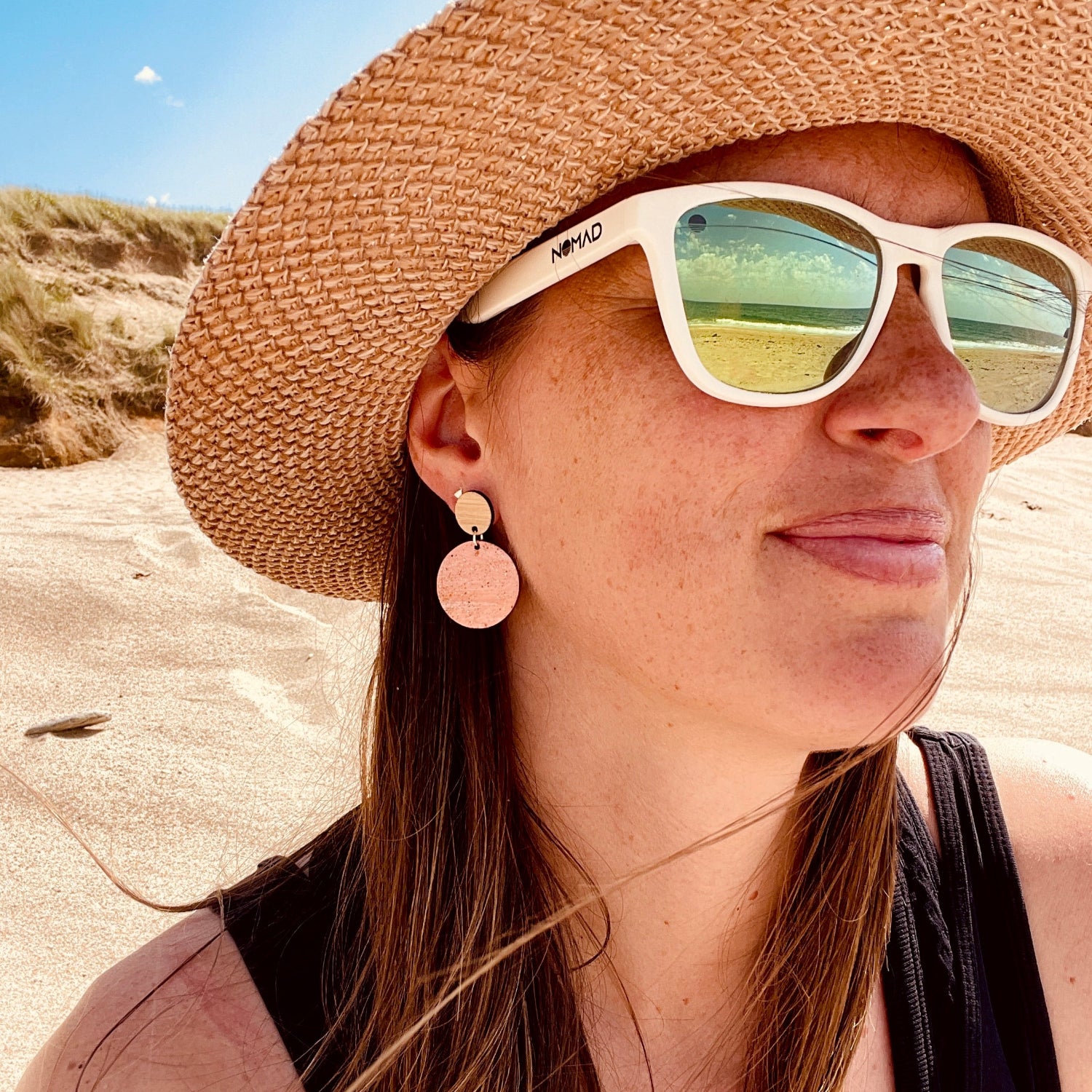 Person wearing a straw hat and sand earrings and sunglasses on a beach