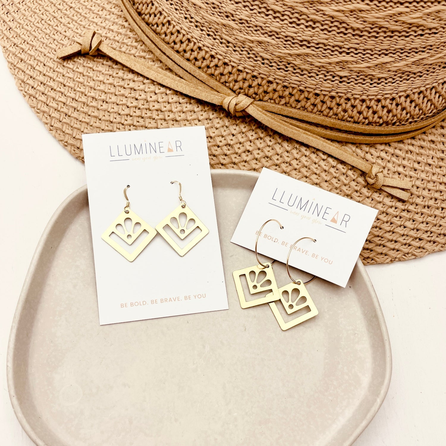 Gold earrings on 'Lluminear' cards with a woven bag in the background