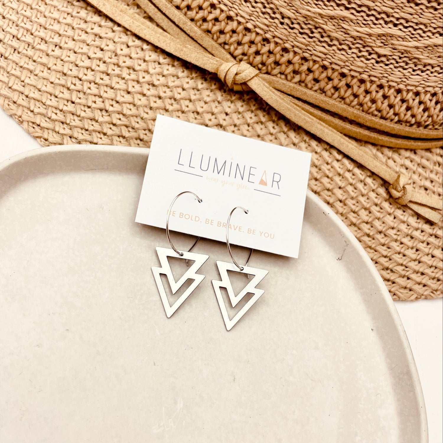 Triangular earrings on a Lluminear branded card with a woven mat in the background
