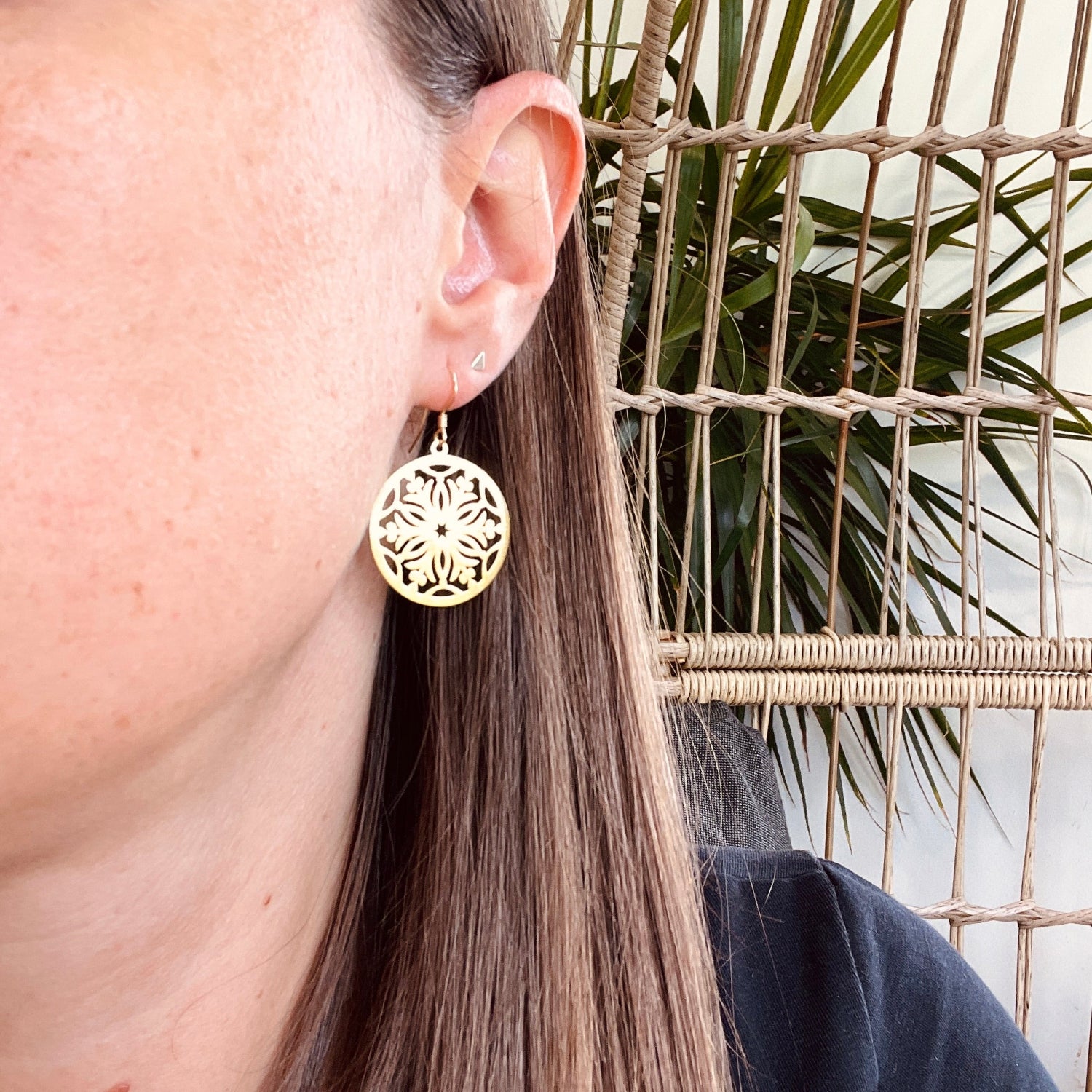 Close-up of a person wearing gold earrings with a plant in the background