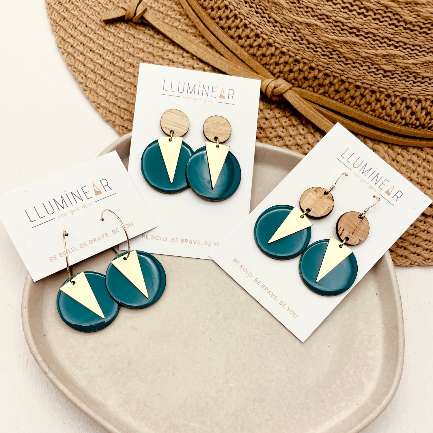Pair of forest green and gold triangle earrings on a white plate with branded cards