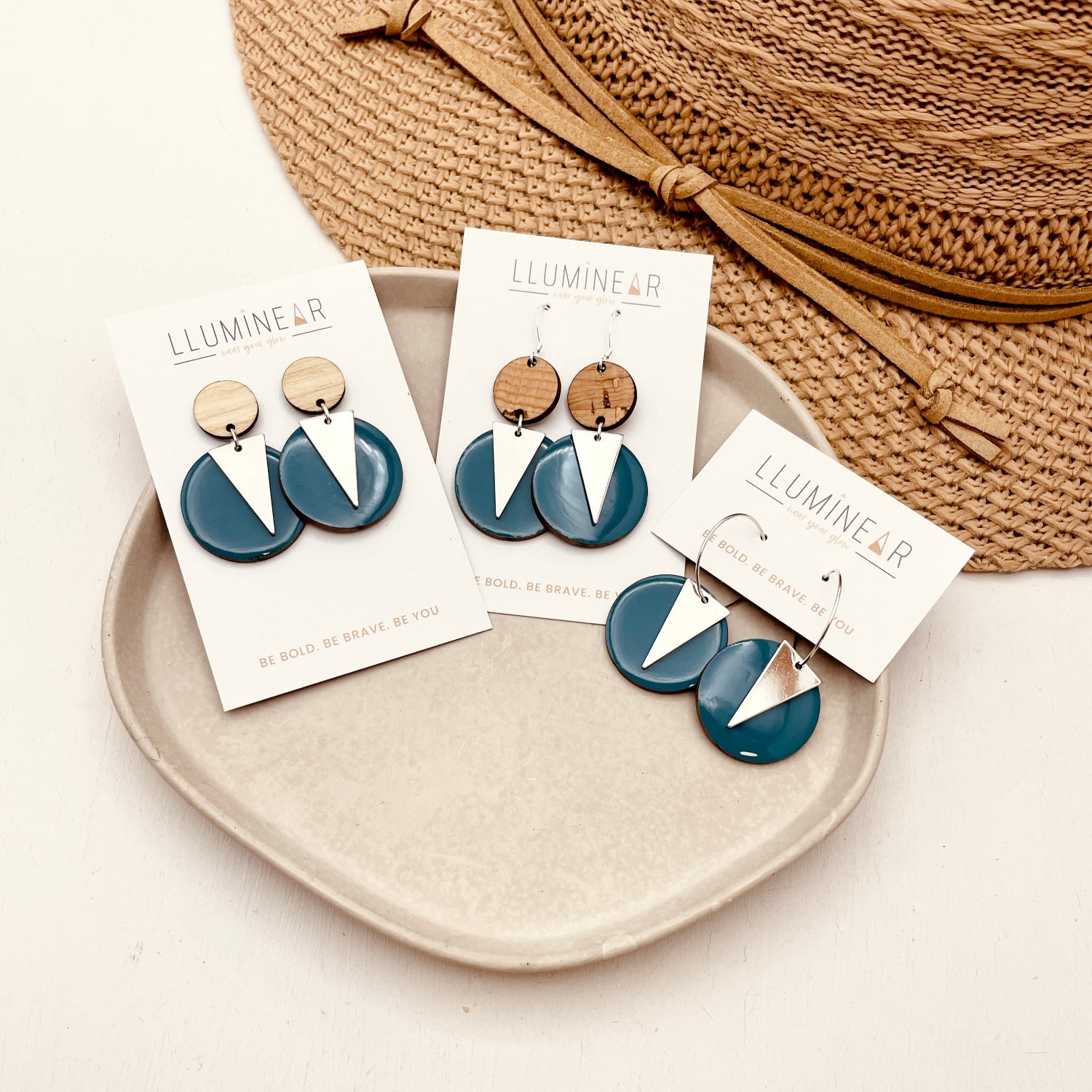Blue and silver earrings on display with branded cards on a beige plate.