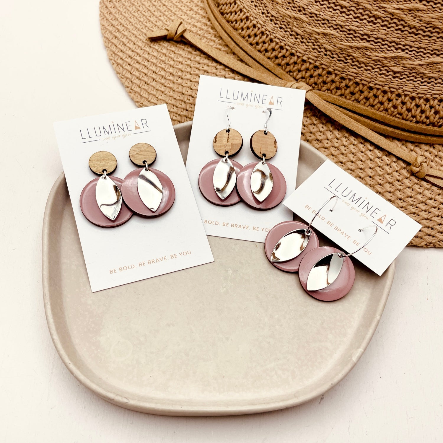 Pair of earrings on display with branded cards on a beige plate, against a neutral background.